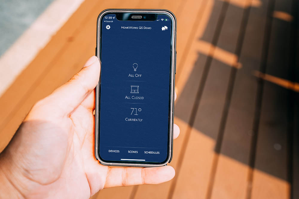 Someone holding their iPhone with the Lutron app to control their home motorized shades and lights.